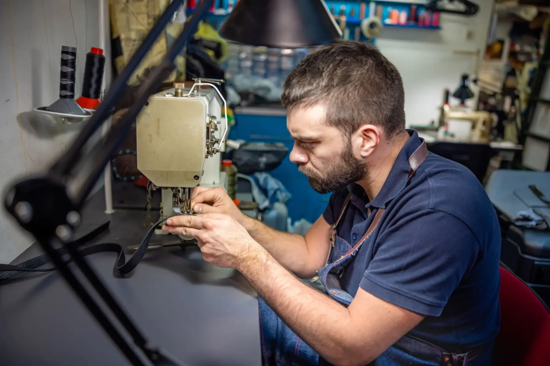 A man sewing fabric on an industrial sewing machine in a workshop.